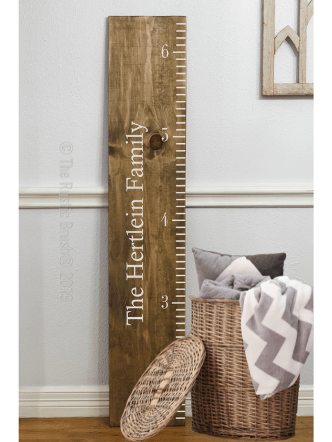 Wooden growth chart ruler with 'The Hertlein Family' next to a wicker basket with a blanket.