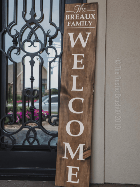 Wooden welcome sign leaning against an ornate black door.