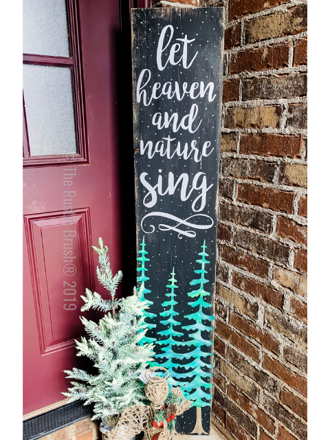 Vertical sign with 'let heaven and nature sing' beside a small pine tree by a door.