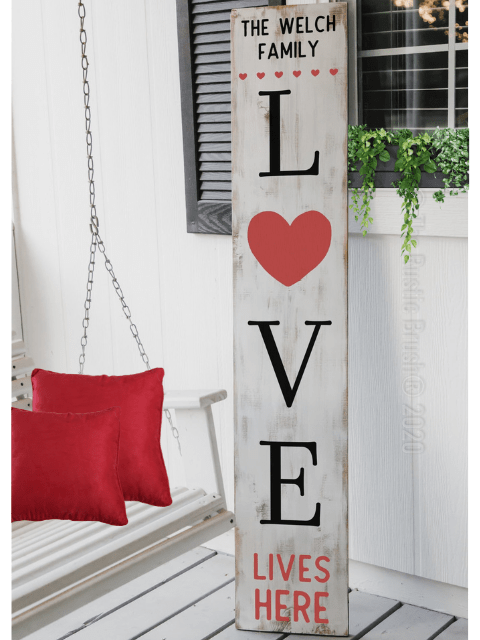 Wooden sign with 'LOVE' text and heart, red cushions, and plant on a porch.