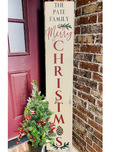 Vertical sign with 'Merry Christmas' by a potted decorative plant.