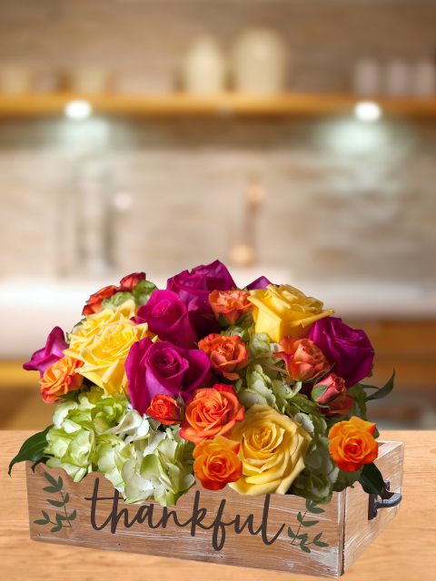 Colorful rose bouquet in wooden box labeled 'thankful' with a blurred kitchen background.