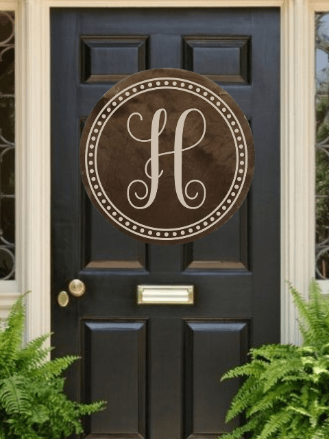 Black door with a circular monogram 'H' and brass mail slot, surrounded by ferns.