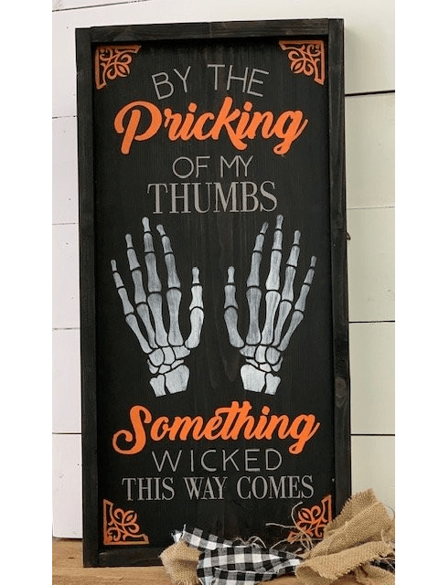 Halloween sign with skeleton hands and spooky text in orange and white on black background.