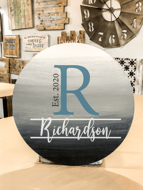 Round wooden sign with letter 'R' and 'Richardson Est. 2020' text, with decorative background.