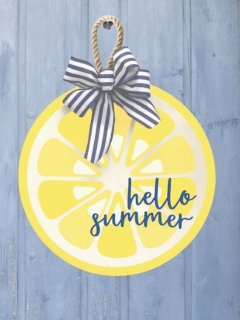 Round lemon sign with 'hello summer' text, striped bow on blue wooden background.