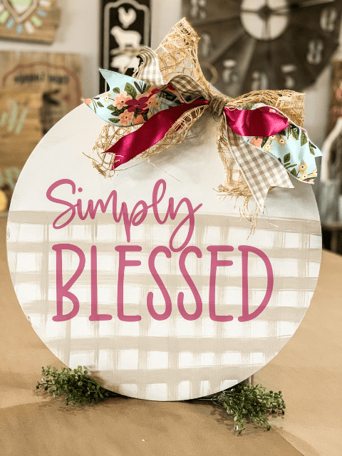 Round decor sign with 'Simply Blessed' text and decorative ribbon on top.