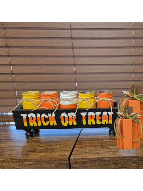 Jars in autumn colors labeled 'Trick or Treat' on a wooden stand with a pumpkin decoration.