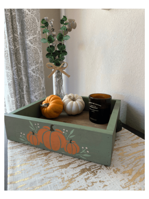 Decorative tray with pumpkins, candle, and plant on a gold-patterned tablecloth.