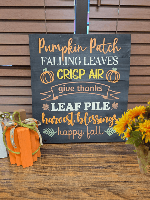 Decorative autumn sign with words like 'Pumpkin Patch', 'Falling Leaves', and 'Happy Fall' next to sunflowers.