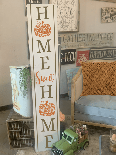 Wooden sign with 'Home Sweet Home', pumpkin design, greenery, seat with orange cushion, decorative truck.