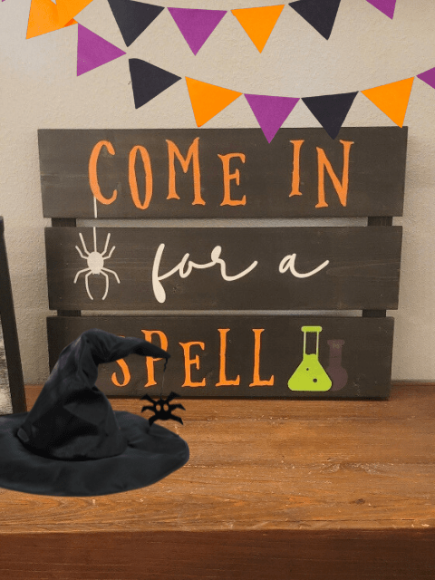 Halloween decor with sign 'Come in for a spell', witch hat, spider, and potion bottles.