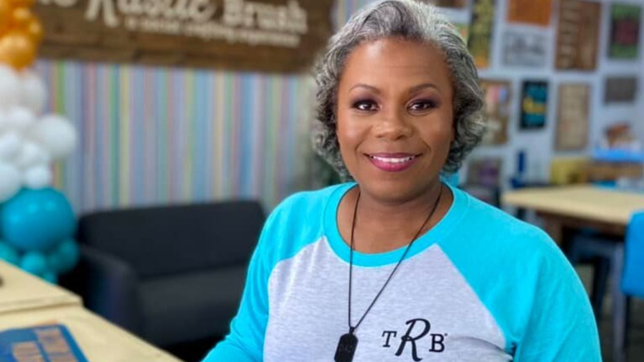 Rhonda Turner’s Stories Smiling woman in a blue and white shirt standing in a colorful room with balloons and wall decorations.