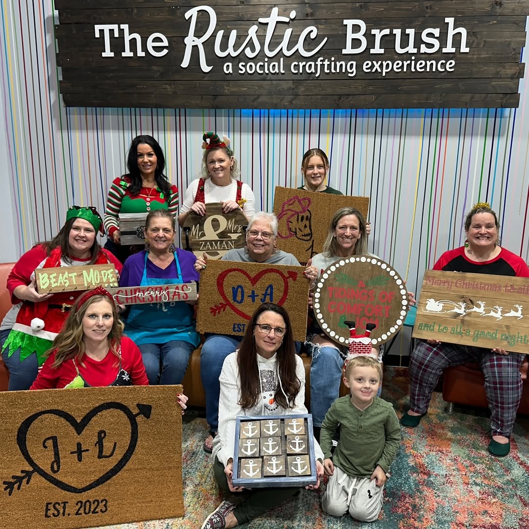 Group of people holding crafted signs at The Rustic Brush with festive decorations.