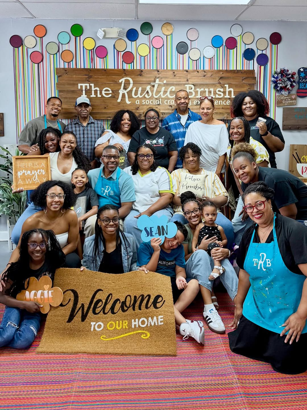 Group posing with signs and doormats inside The Rustic Brush craft studio.