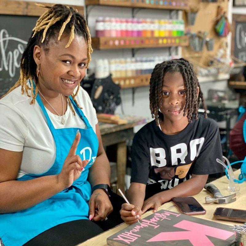 Man and girl smiling in aprons, sanding wood at a craft workshop.