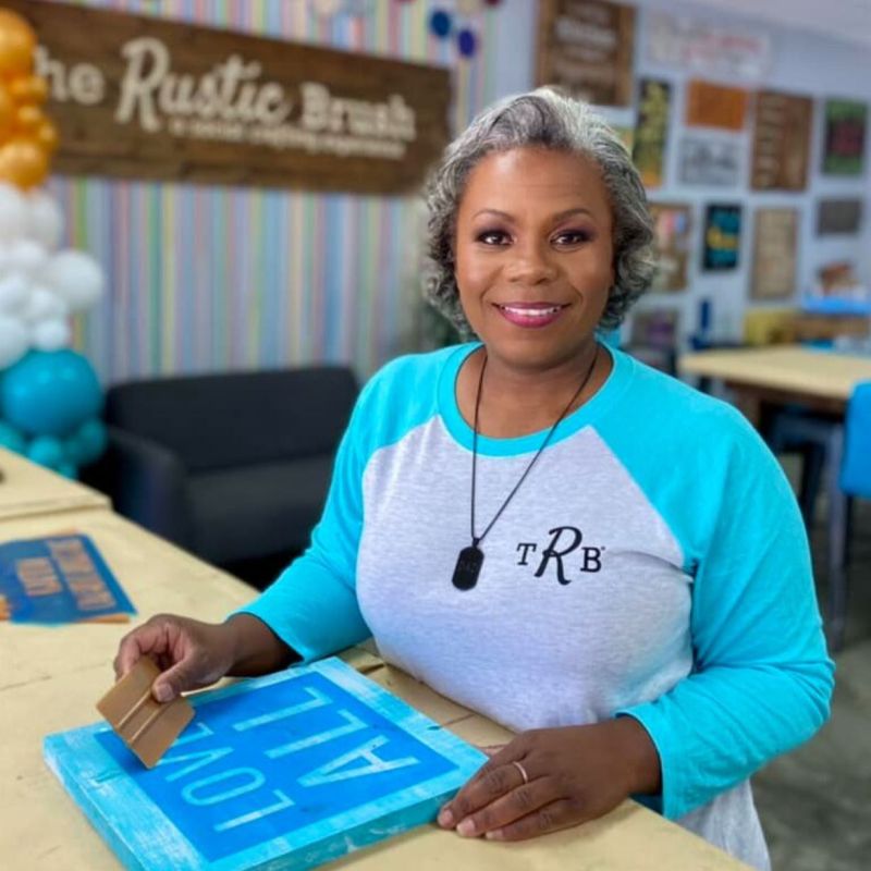 Group of people posing in a craft studio with colorful decor and signs.