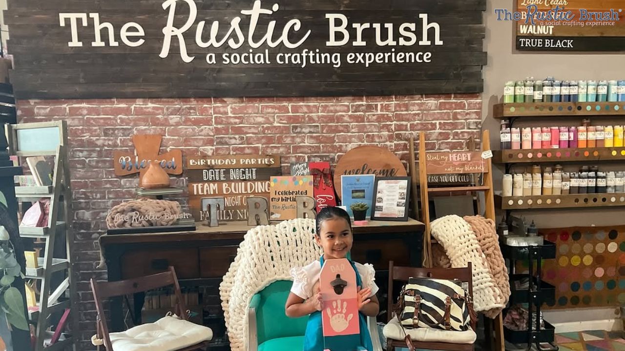 Girl holding craft at The Rustic Brush with paints and decor displayed around.