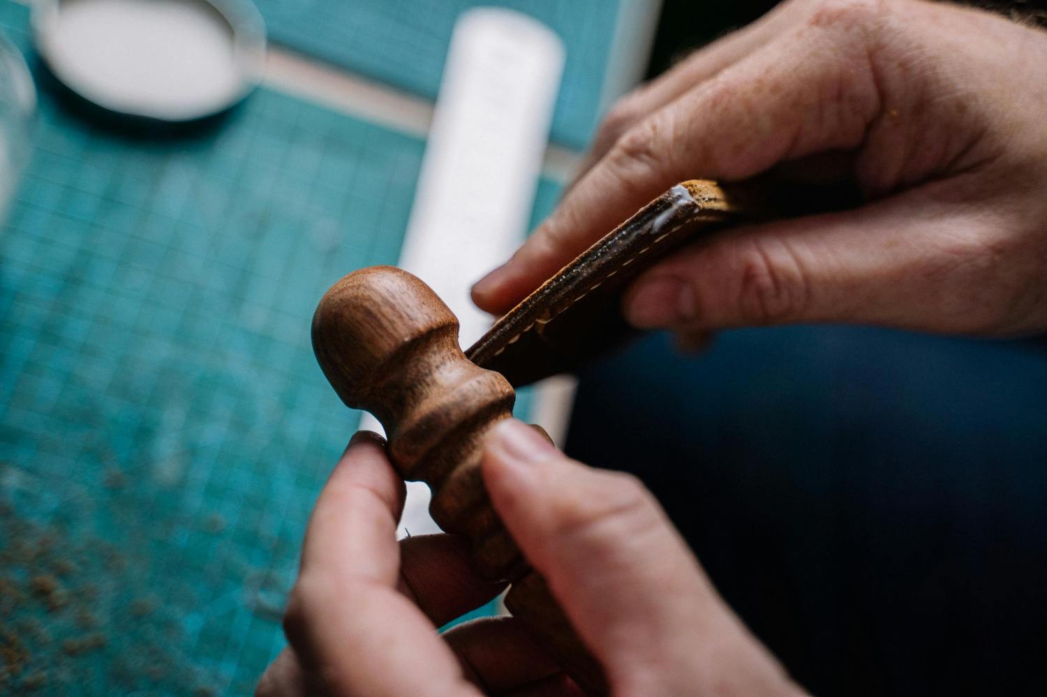 Hands crafting leather with a wooden tool on a green surface.