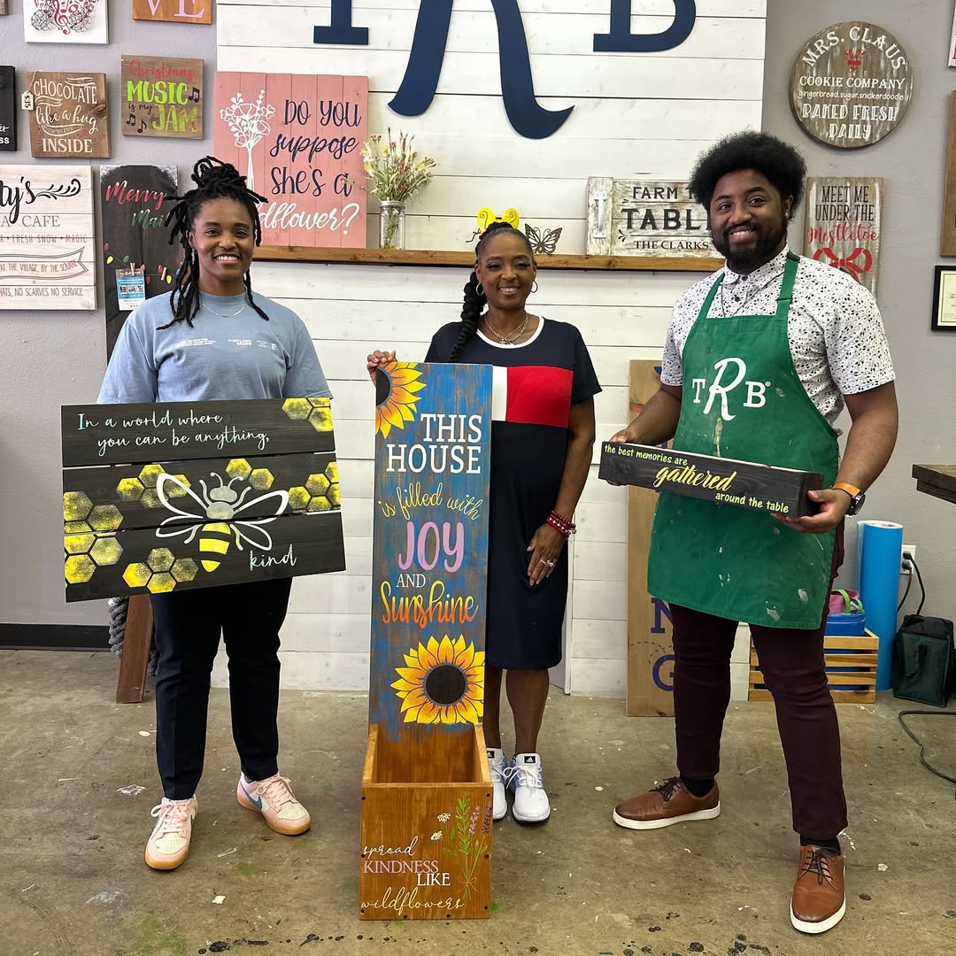 Three people holding painted signs with positive messages in a decorative room.