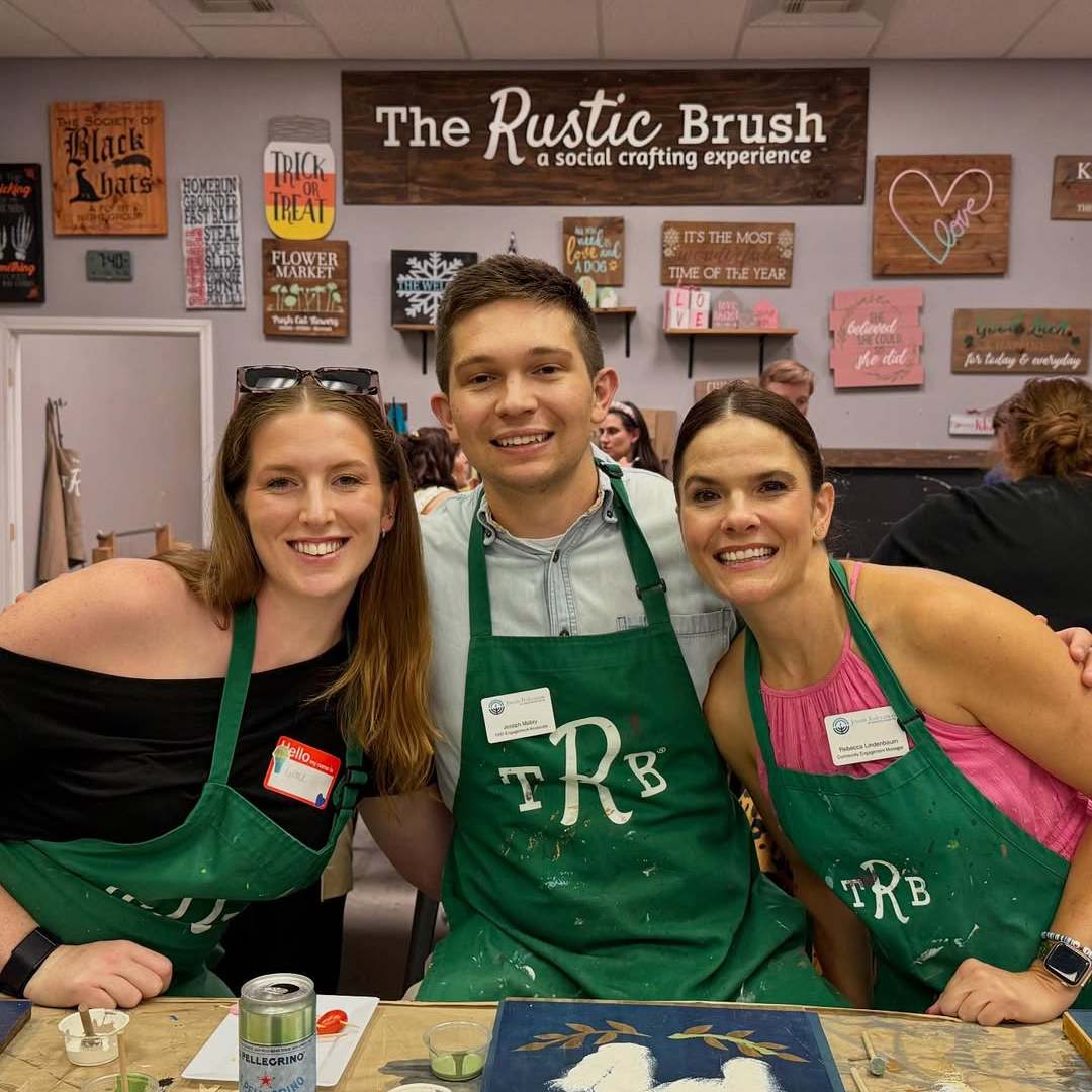 Three people wearing green aprons smiling at a crafting event.