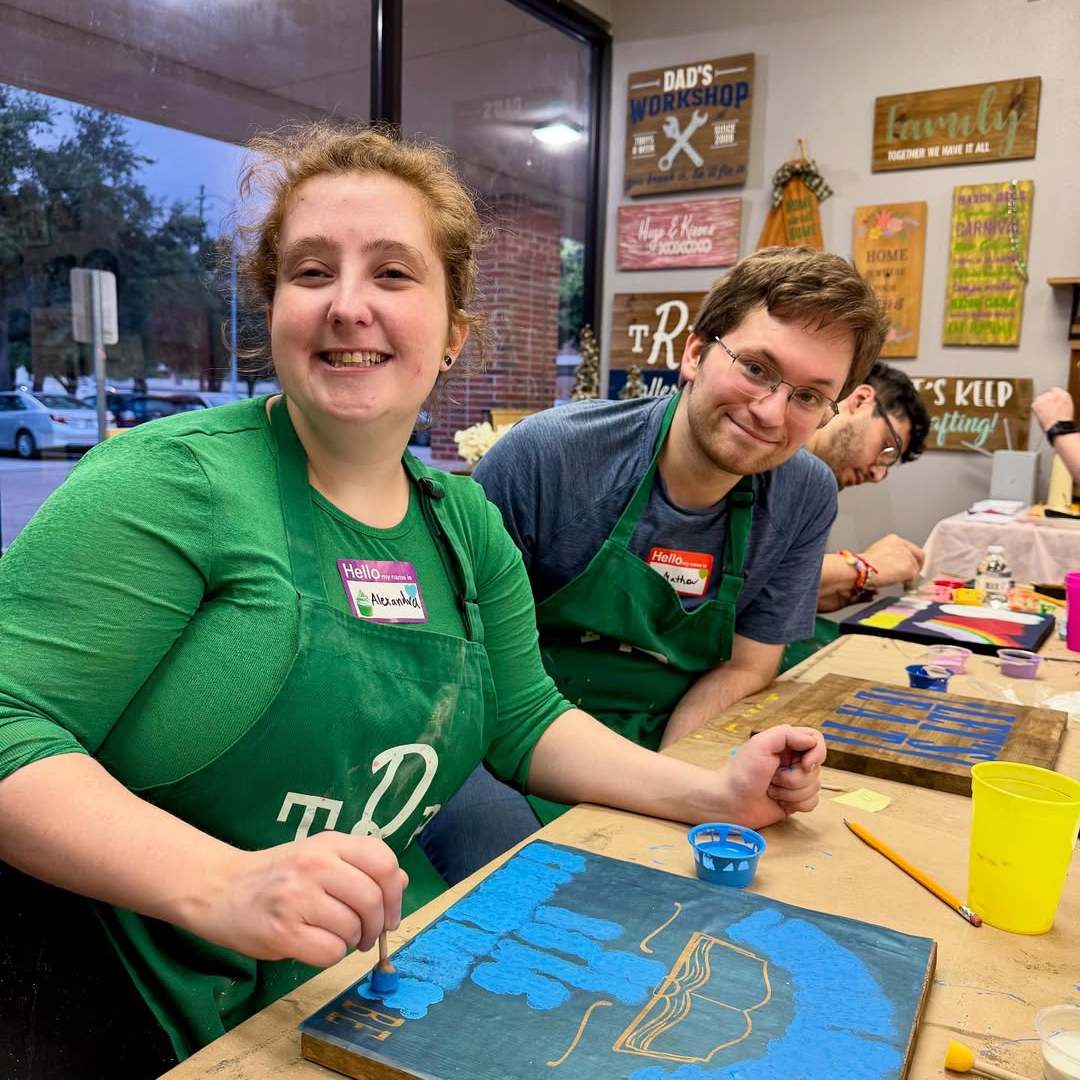 Two people smiling while painting at a craft workshop.