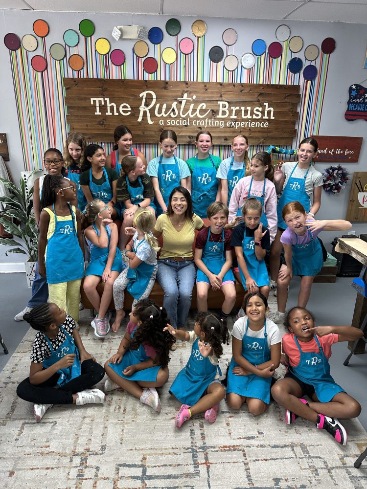 Group of children and an adult posing at The Rustic Brush with colorful wall decor.