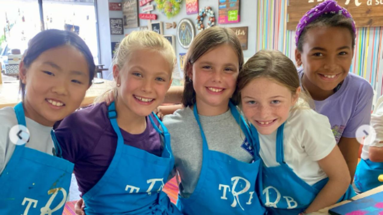 Five smiling girls in blue aprons posing together indoors.