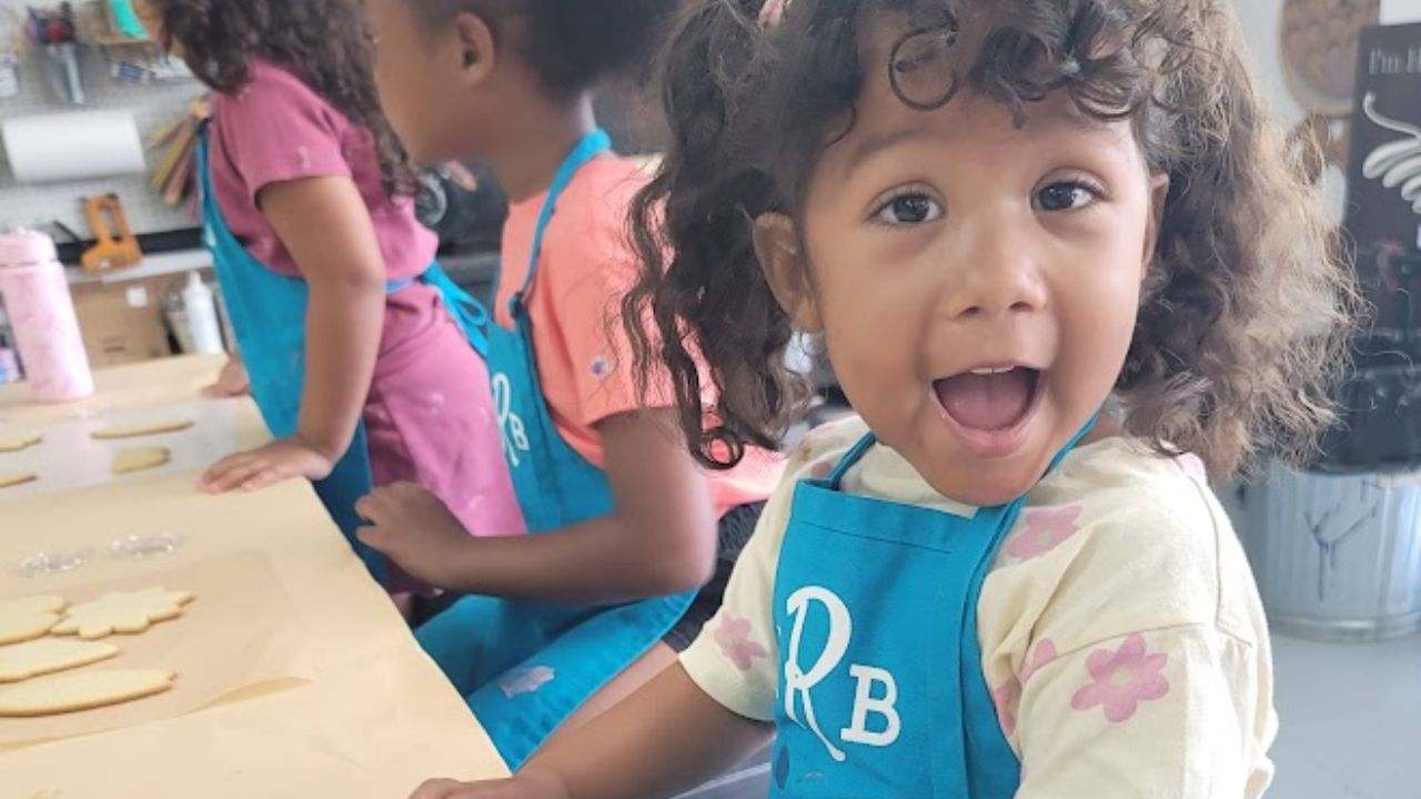 Three children in blue aprons crafting at a table, with one looking surprised.