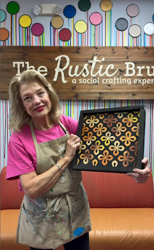 Person holding painted artwork with flowers in crafting space.