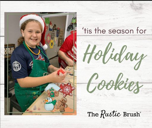Smiling child in santa hat decorates holiday cookies at table, text reads 'Holiday Cookies' from 'The Rustic Brush'.