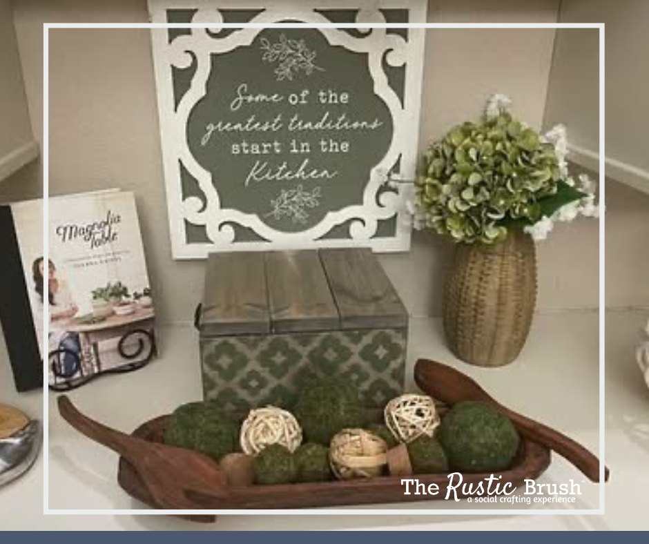 Decorative kitchen items: vase, sign, book, box, and bowl of moss balls on a shelf.