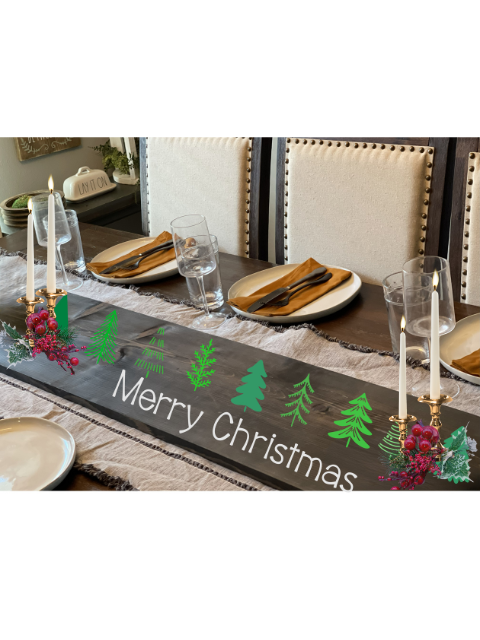 Festive dining table set with 'Merry Christmas' runner, candles, and pine decor.
