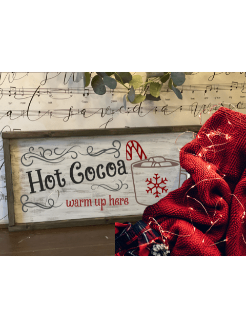 Hot Cocoa sign with candy cane, red blanket, and fairy lights on music sheet background.