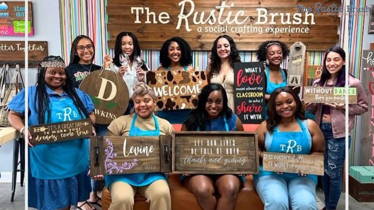 A group of people holding personalized wooden signs at The Rustic Brush crafting studio.