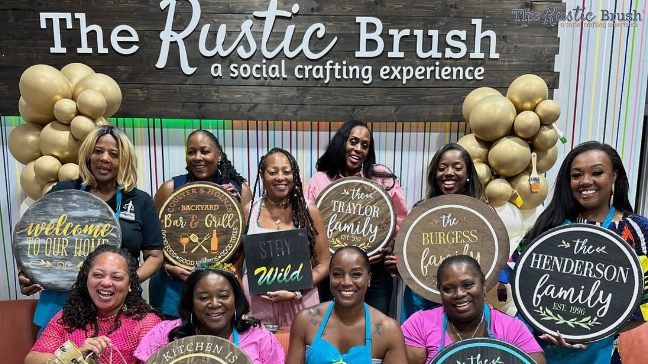 Group of women holding crafted signs at 'The Rustic Brush' with balloons.