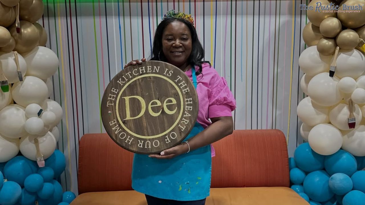 Smiling person holding a round sign with 'The kitchen is the heart of our home.' surrounded by balloons.