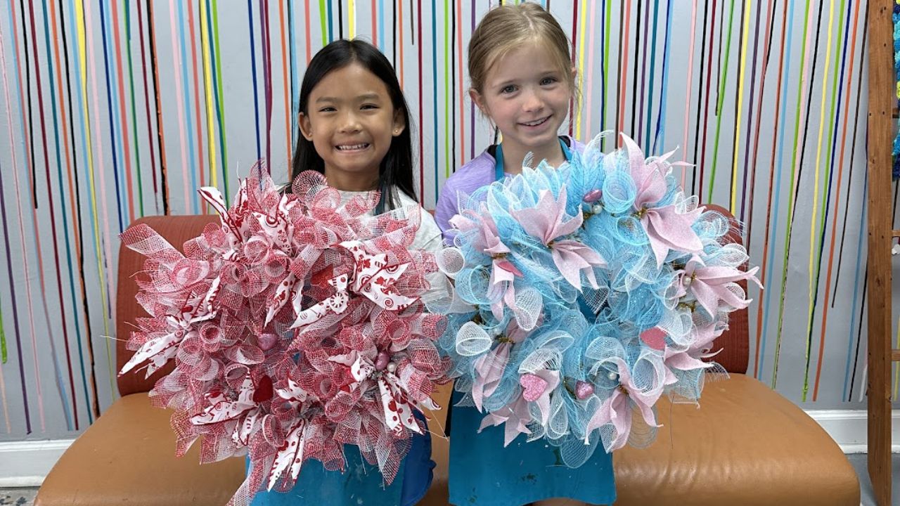 Two girls holding decorative wreaths, one pink and one blue, against a colorful striped background.