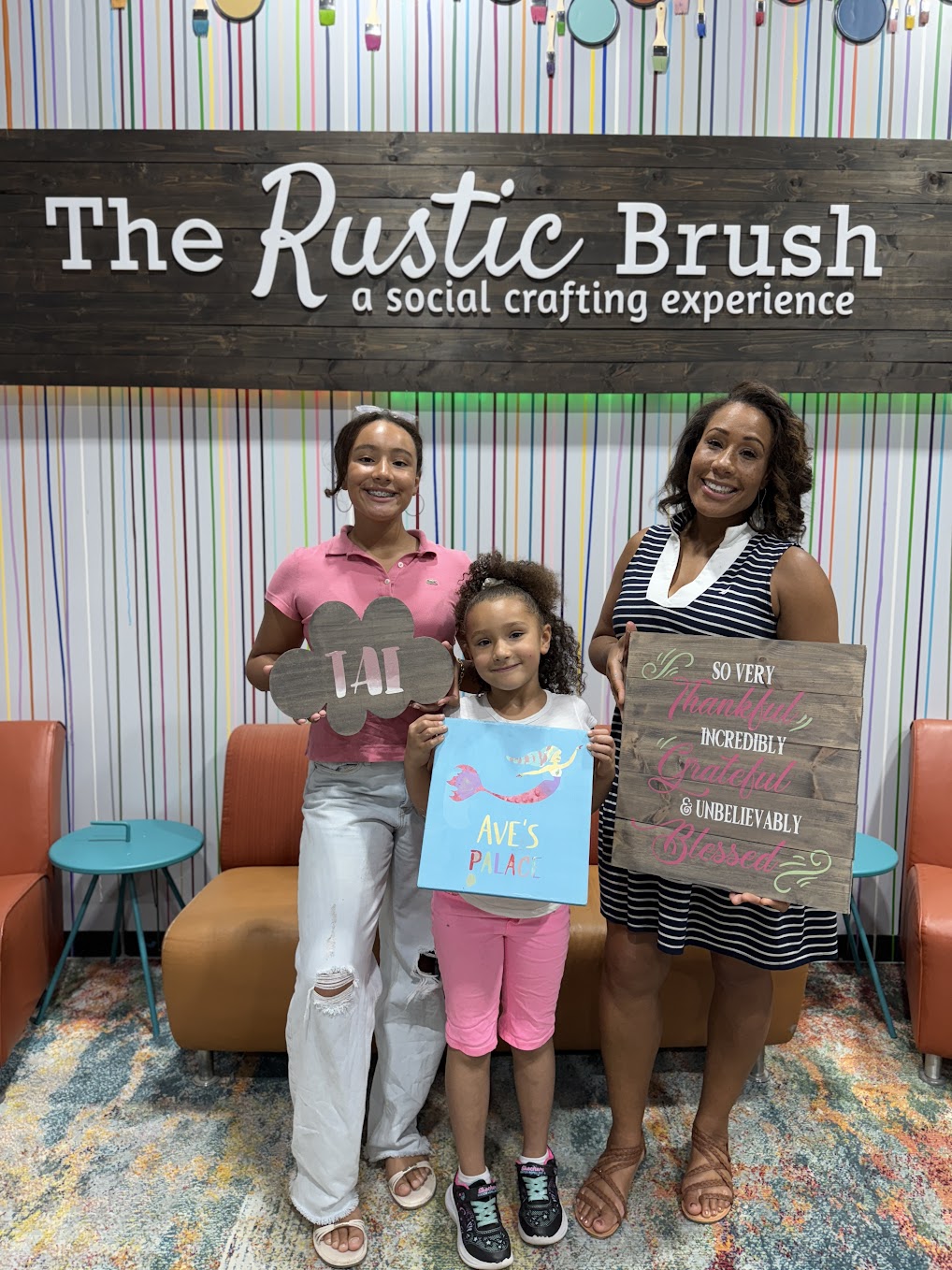 Children and parent showcasing finished DIY craft projects at The Rustic Brush Houston studio.