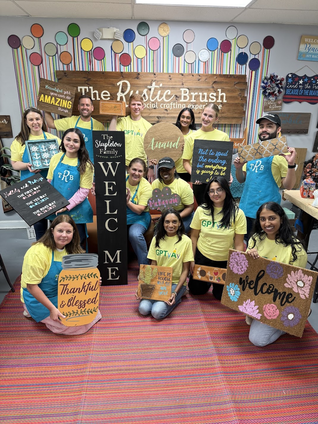 Group holding crafted wooden signs inside The Rustic Brush workshop.