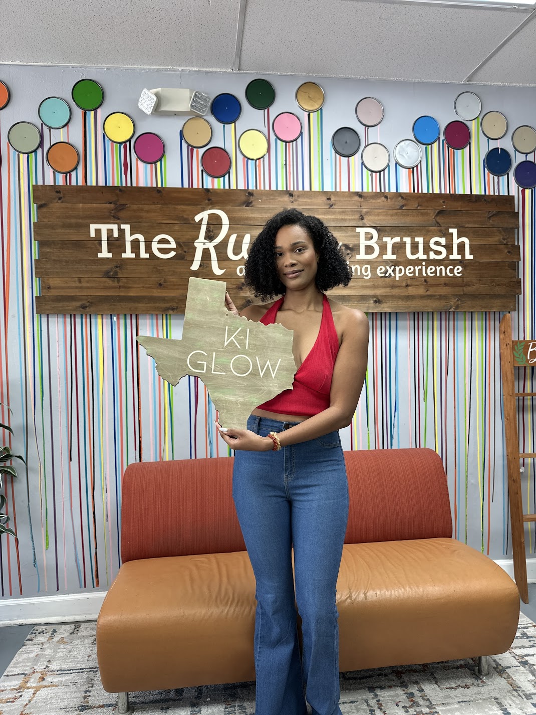 Woman holding a Texas-shaped wooden sign during a DIY workshop at The Rustic Brush.