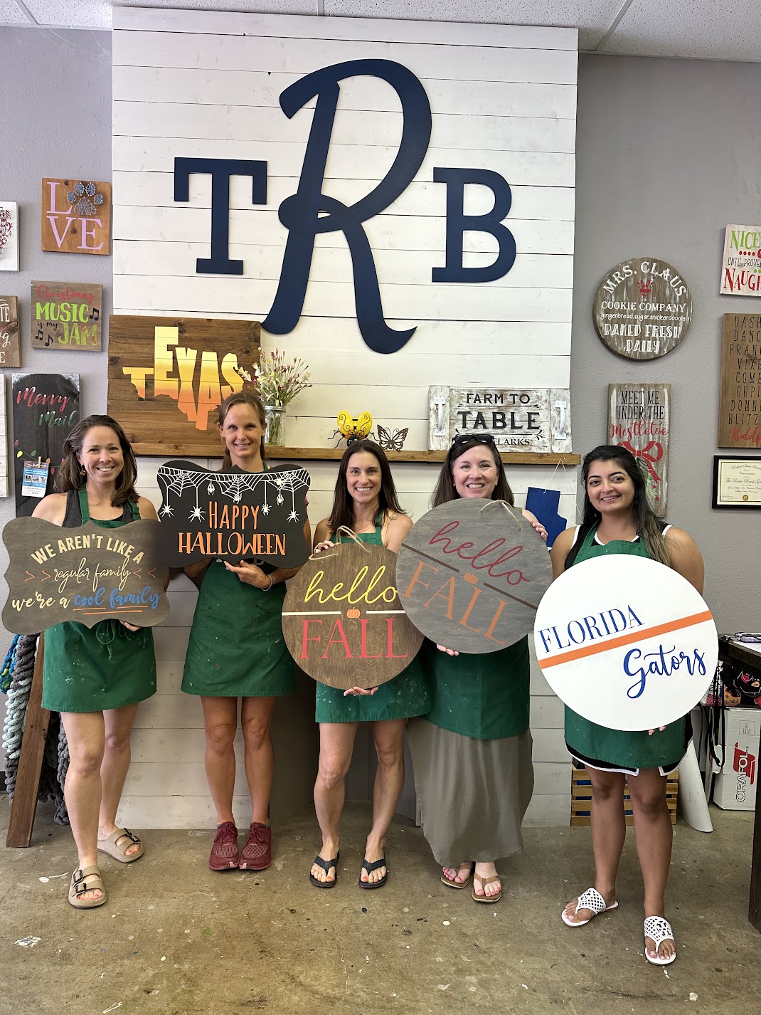 Five women in aprons holding decorative signs under large letters TRB.