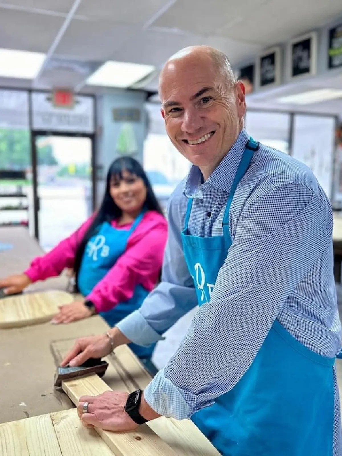 A man sanding a wooden board at a DIY workshop table