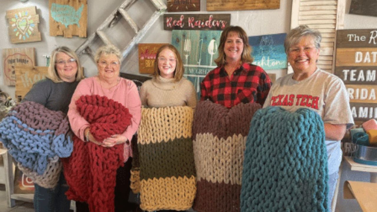 Group of women holding handmade chunky knit blankets inside The Rustic Brush