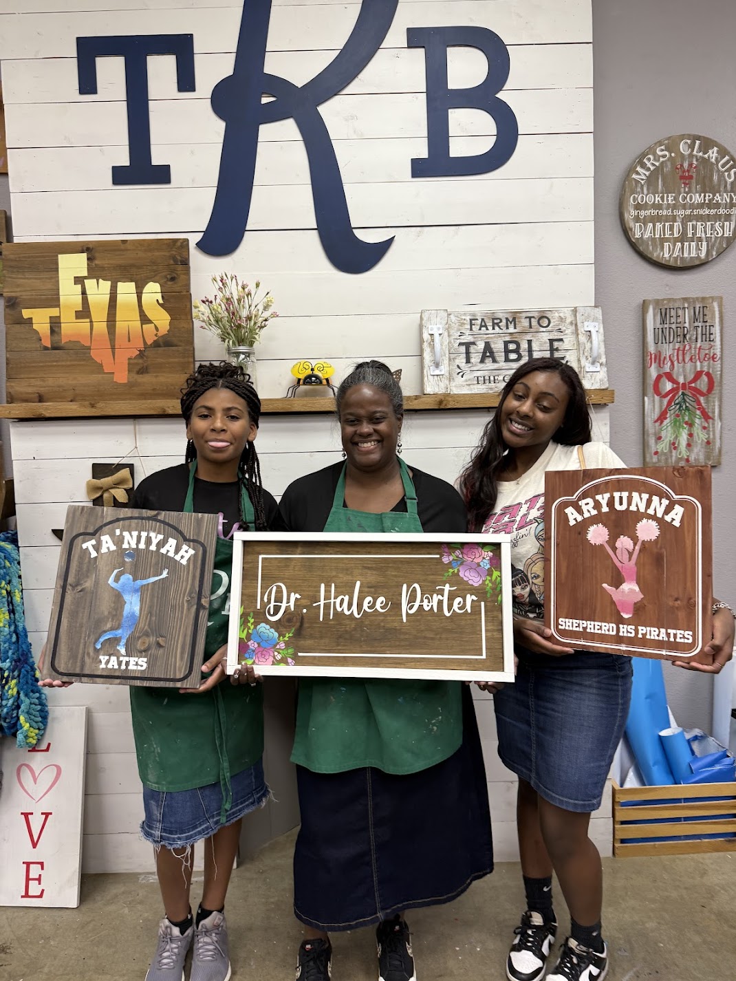 Three people holding personalized wooden signs they created at The Rustic Brush DIY workshop.