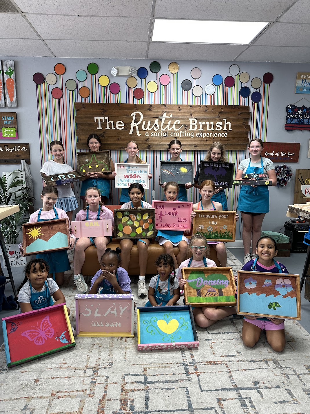 Kids displaying painted wooden tray projects at The Rustic Brush workshop
