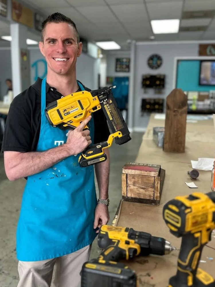 Man in a crafting studio holding a nail gun doing a DIY project.