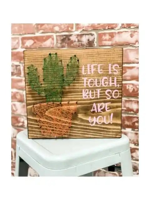 Handmade cactus string art piece on a wooden board with a motivational quote.
