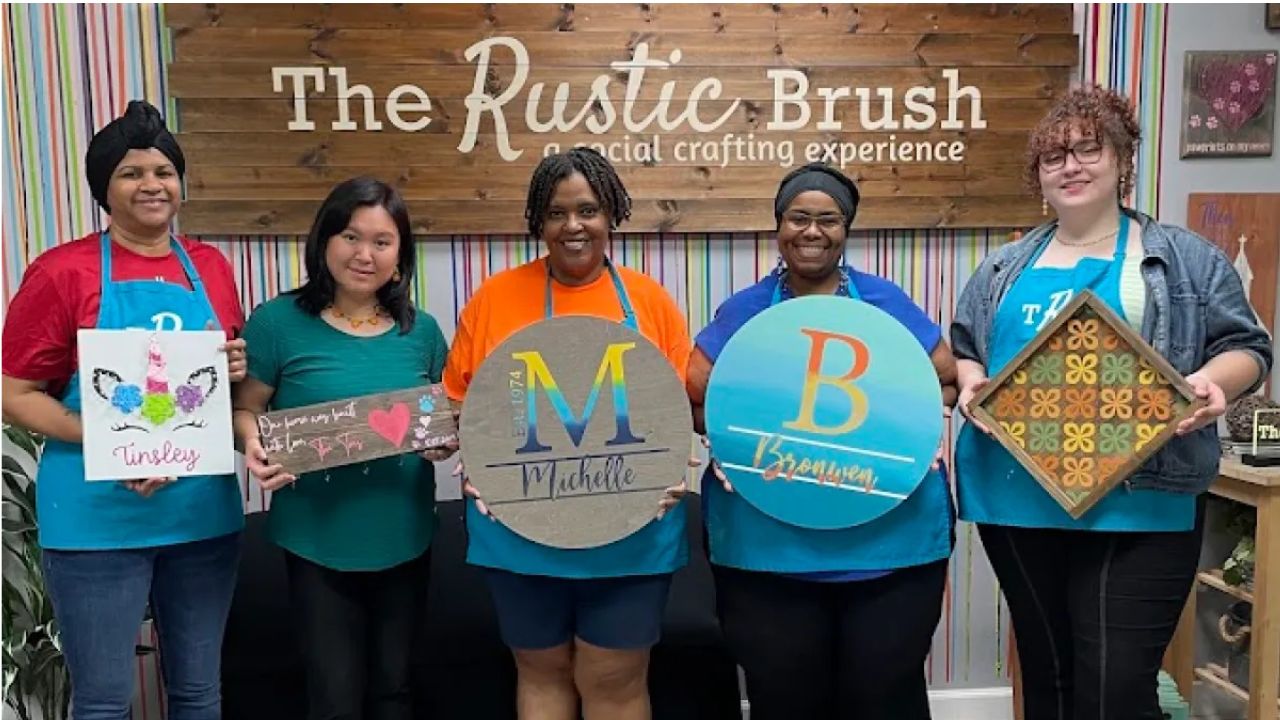 Participants holding their finished DIY signs at The Rustic Brush workshop.
