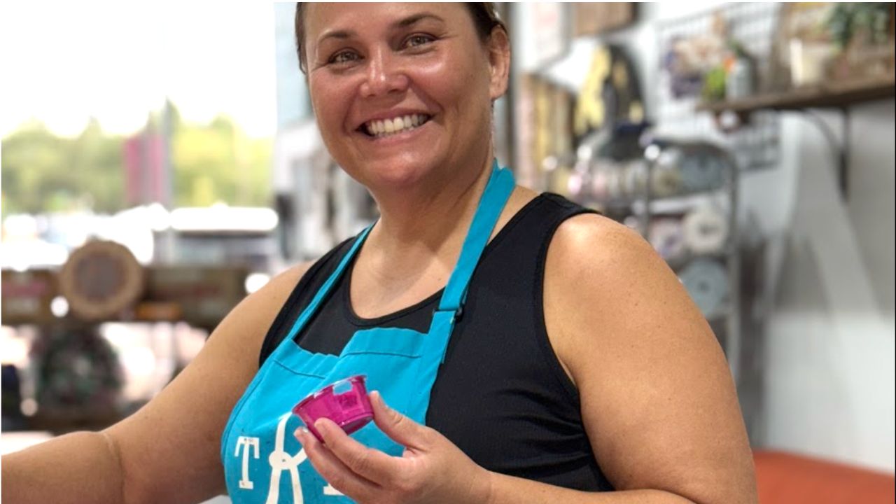 Smiling woman in an apron painting a colorful wooden board at The Rustic Brush